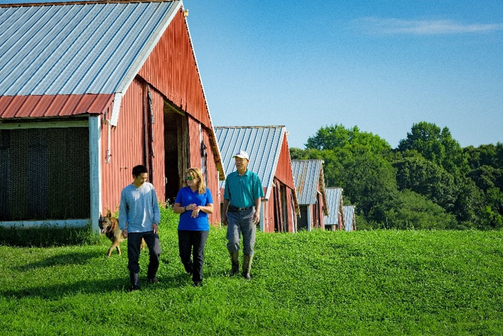 Three people and dog walking in front of barn