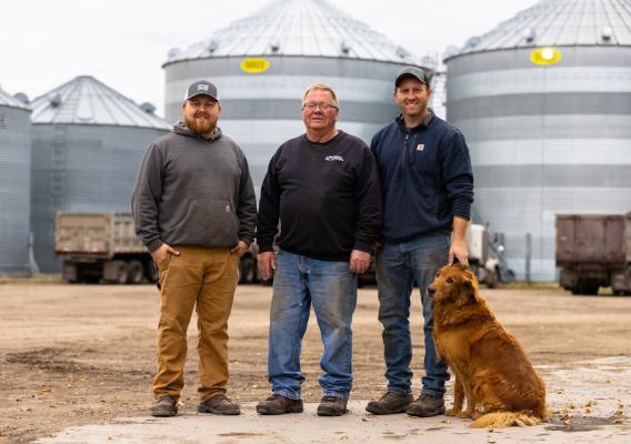 Three people and dog standing in front of silos