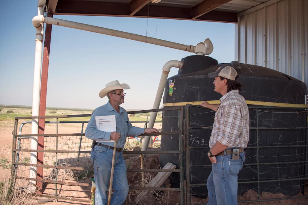 Kregg McKenny (left) and Derrick Fuchs (right) discuss Kregg’s grazing plan next to one of his water storage tanks from his rainwater harvesting system