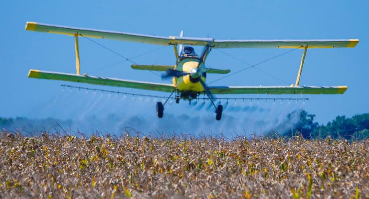 "A crop duster plane showers a field with fungicide and insecticide"
