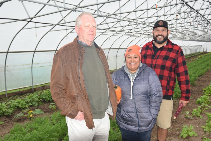 Two men and a woman pose with a squash in a high tunnel.