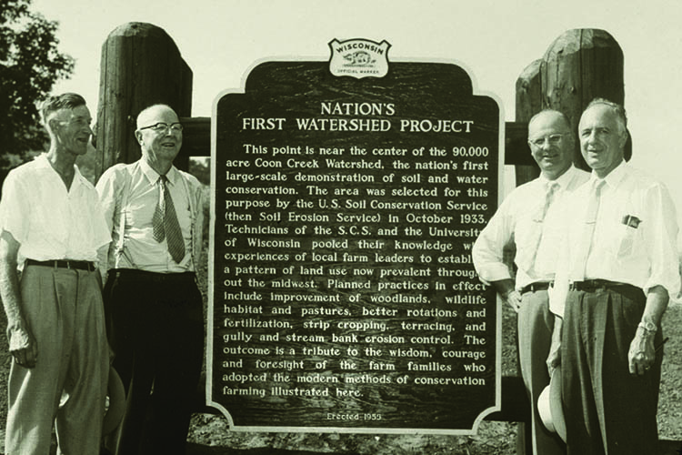 Dr. Hugh Hammond Bennett (second from left), first Chief of the former Soil Conservation Service, stands with former SCS officials next to a watershed project historical marker commemorating the nation’s first large-scale soil and water conservation project in Coon Valley, Wisconsin. 