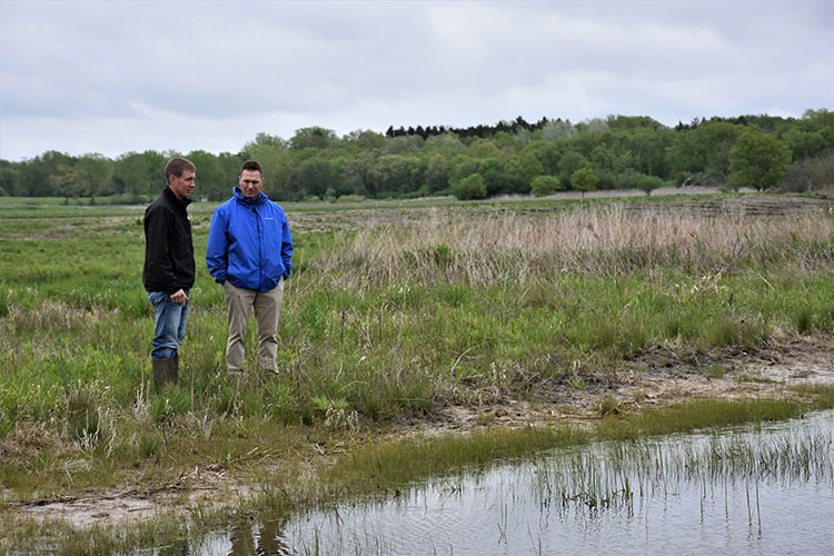 (L to R) Caleb Zahn and TJ Rogers view one of the successful wetland scrapes on the easement, added to hold excess water, while also creating wildlife habitat and attracting different species. Photo taken in 2017. 