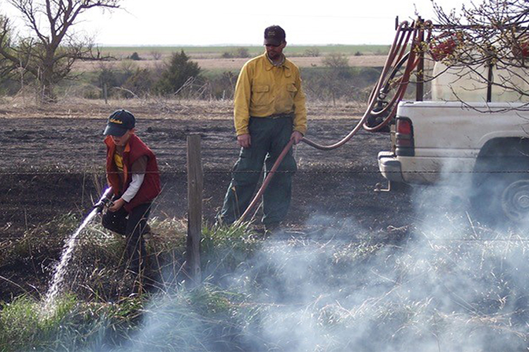 Father and son use water hose to douse controlled burn