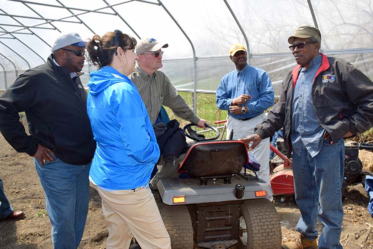 Five people standing around small tractor under a canopy