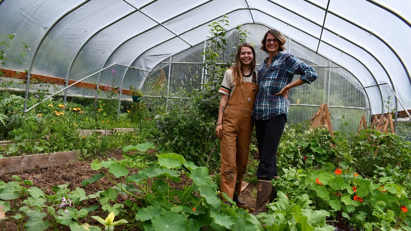 Two women in high tunnel surrounded by green plants. 
