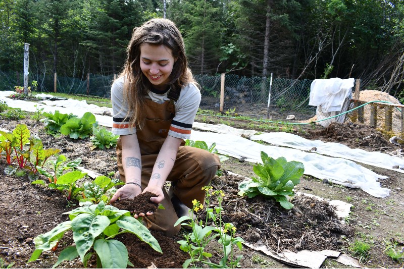 Women kneeling holding soil in a garden with plants.