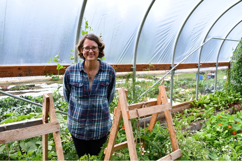 Woman standing in a high tunnel surrounded by green plants. 