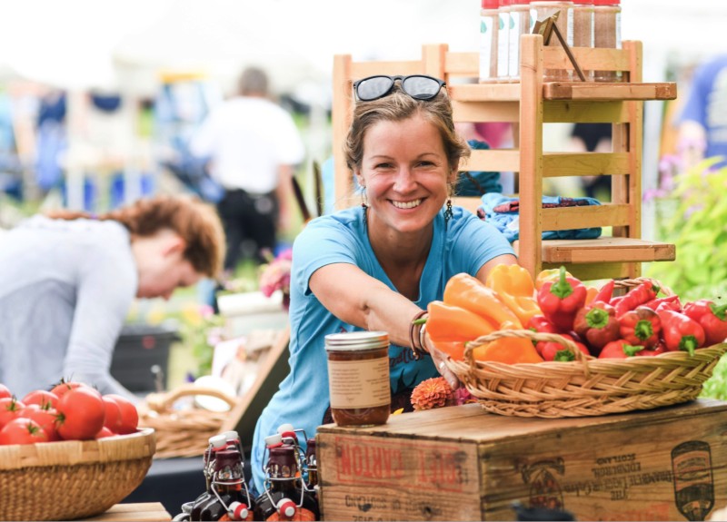 Woman smiling at a vegetable stand holding peppers.