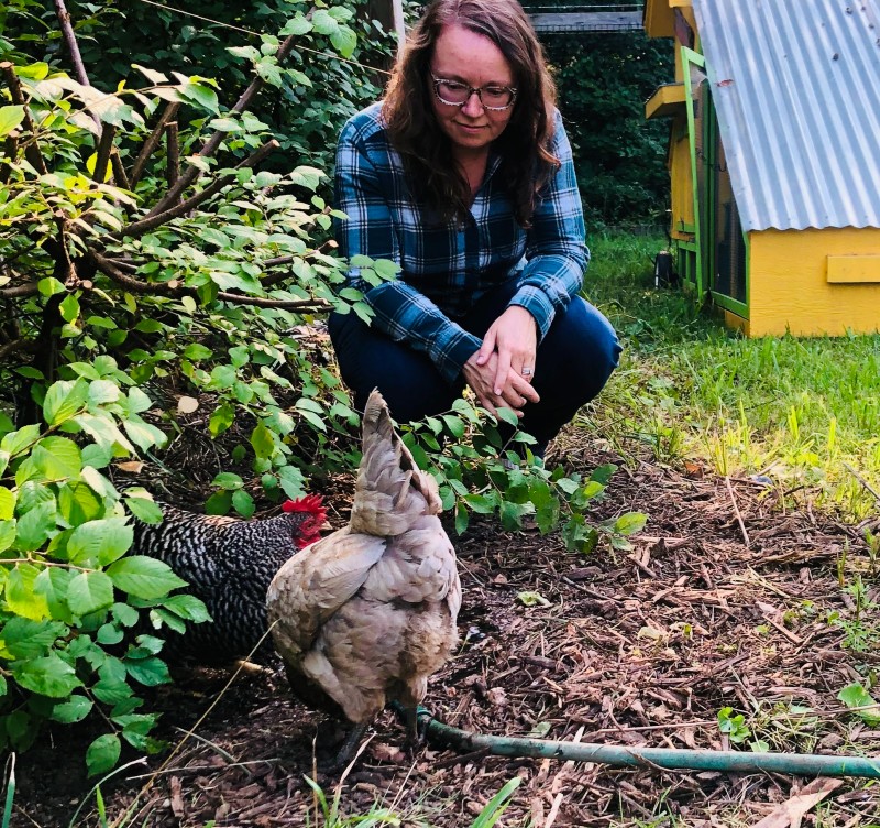 Woman kneeling in a garden watching two chickens feed.
