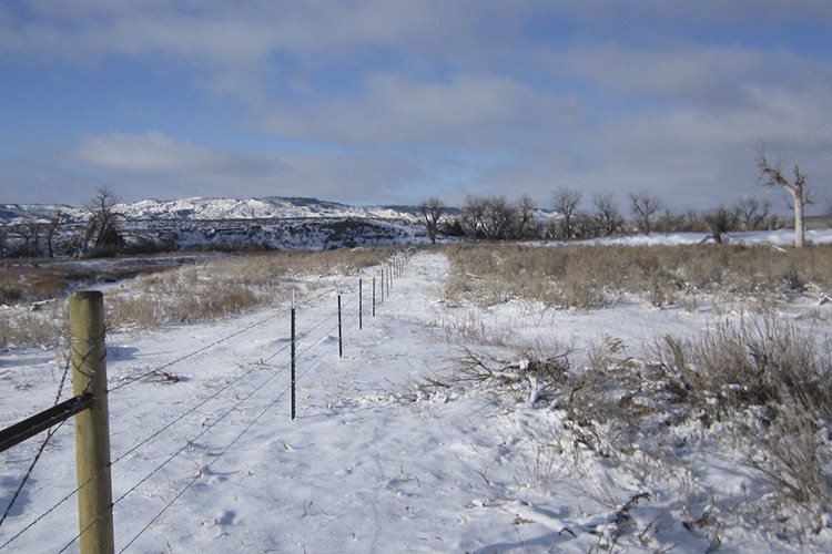 A finished fence line with ground covered in snow. 