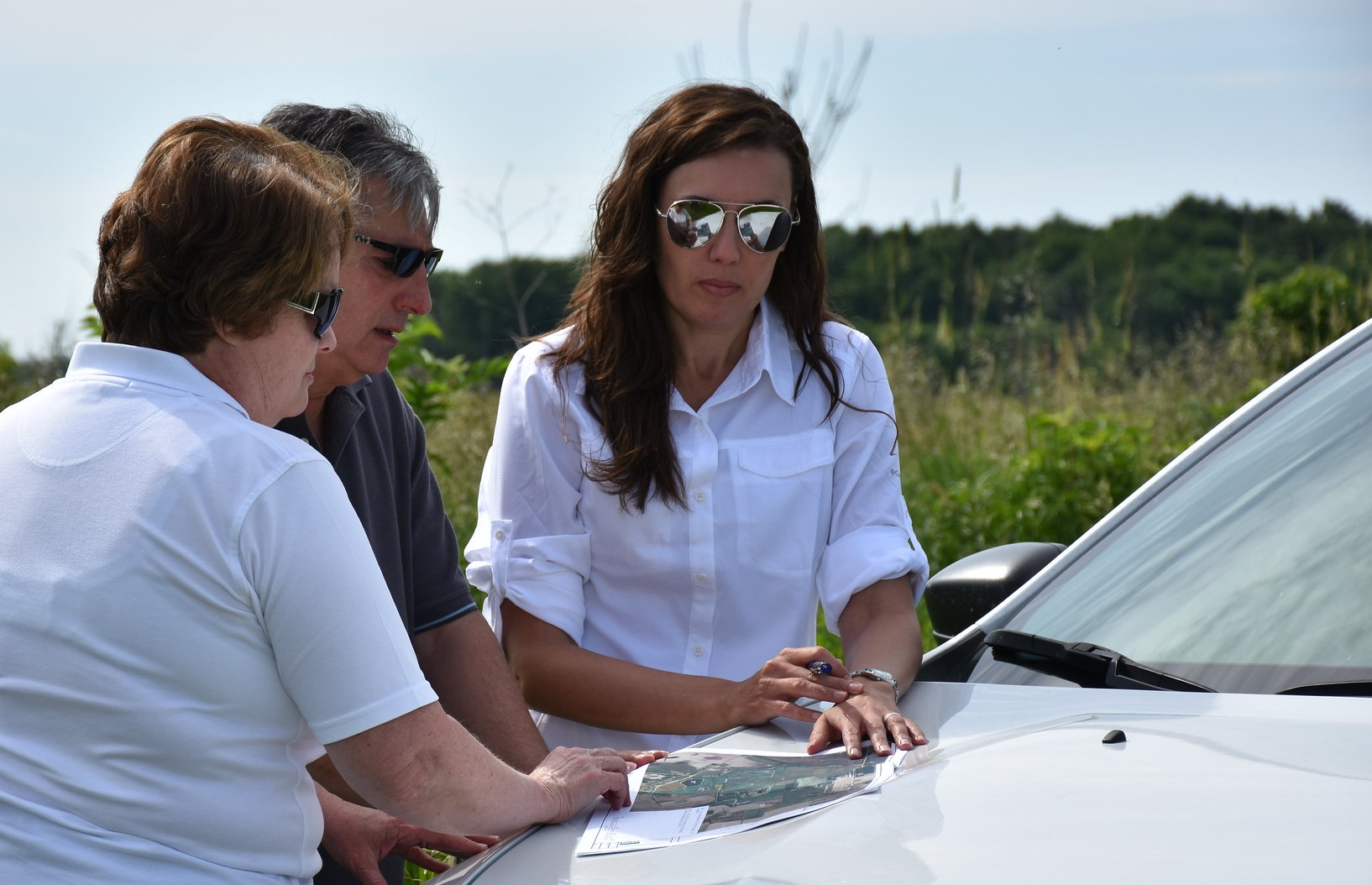 Three people reviewing a map while leaning on the hood of a pick-up truck