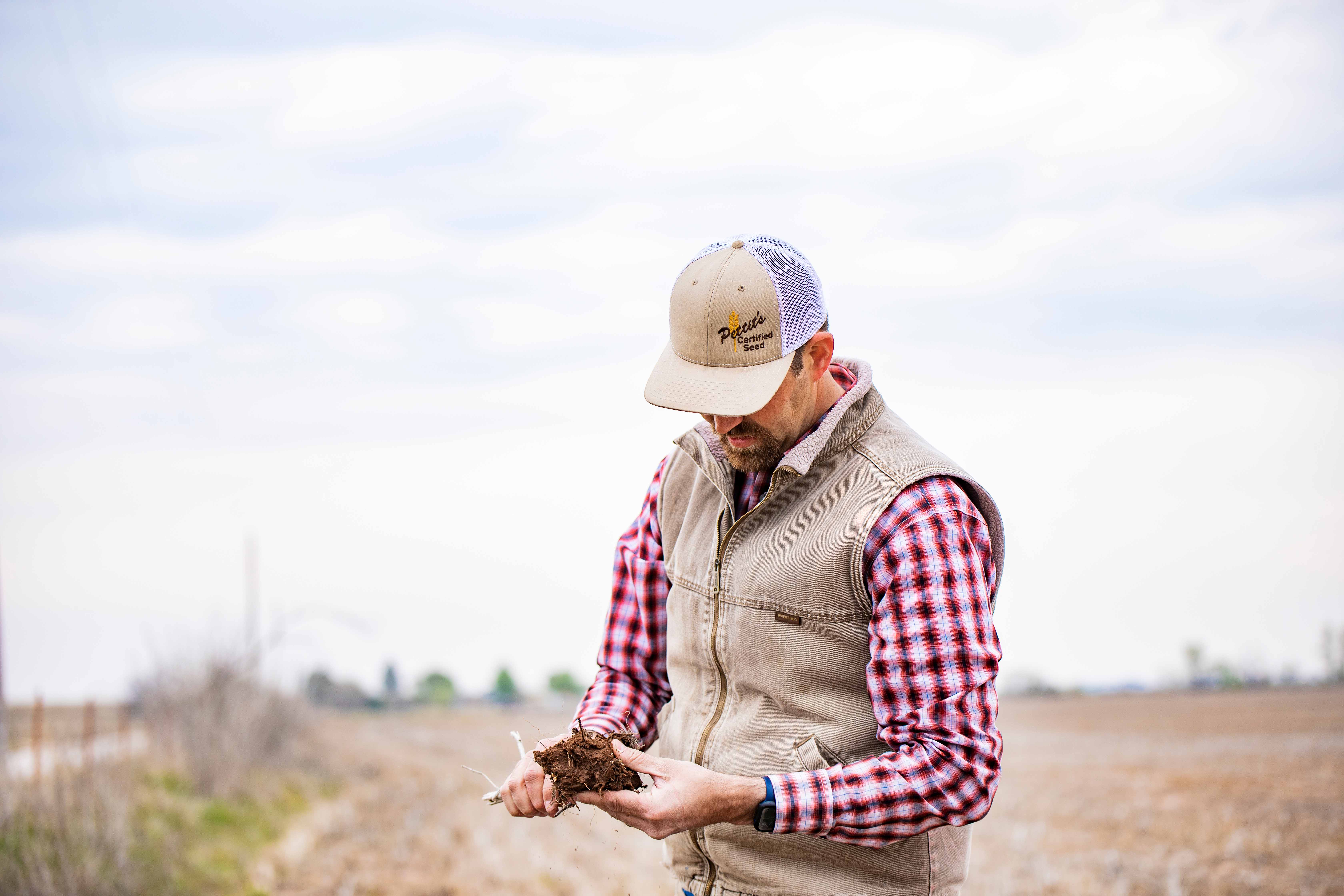 Person standing on dirt road holding dried crop pulled from field