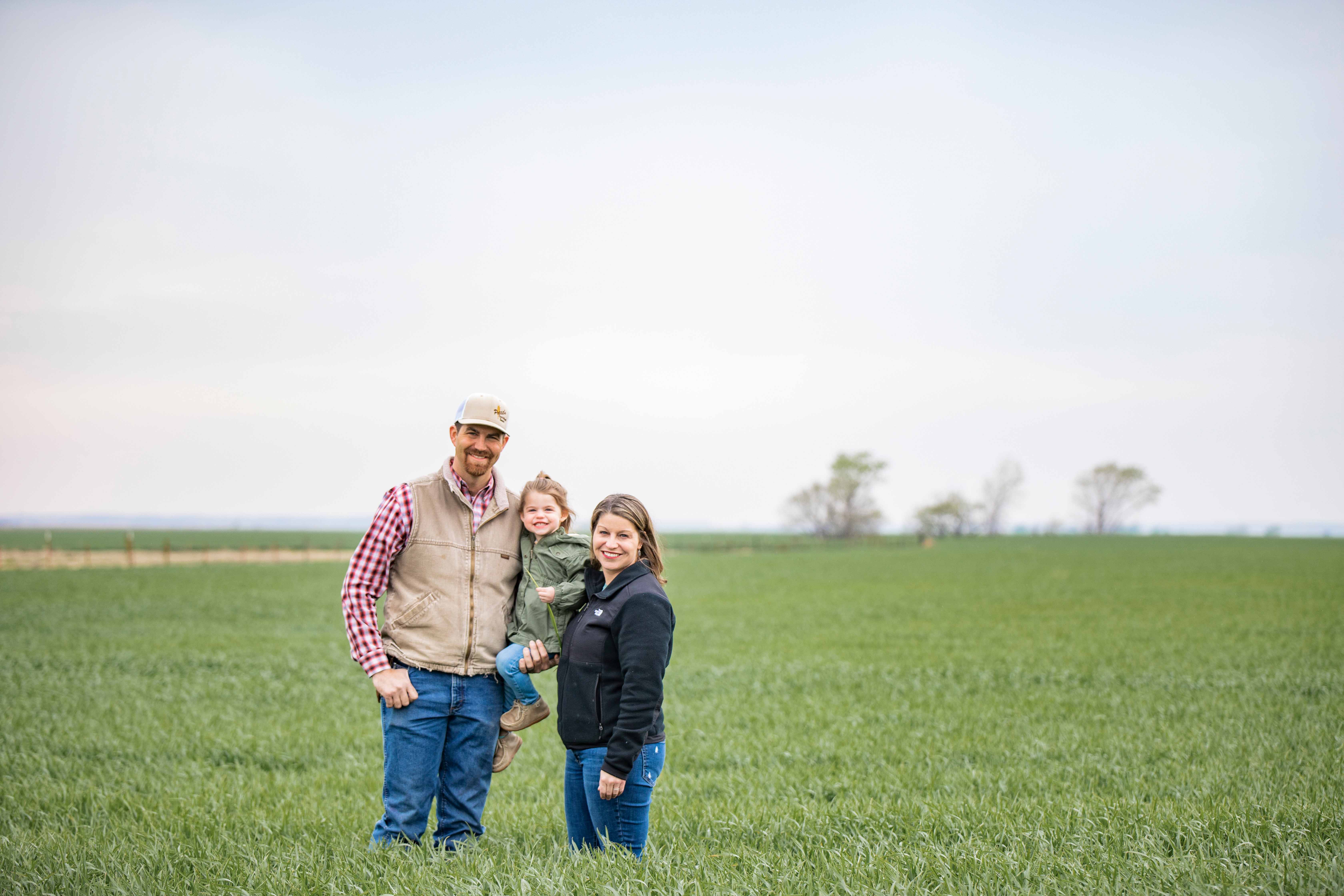 Two people and a child standing in a field smiling