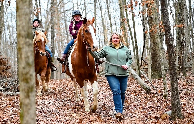 Two people on horses with one person guiding the two