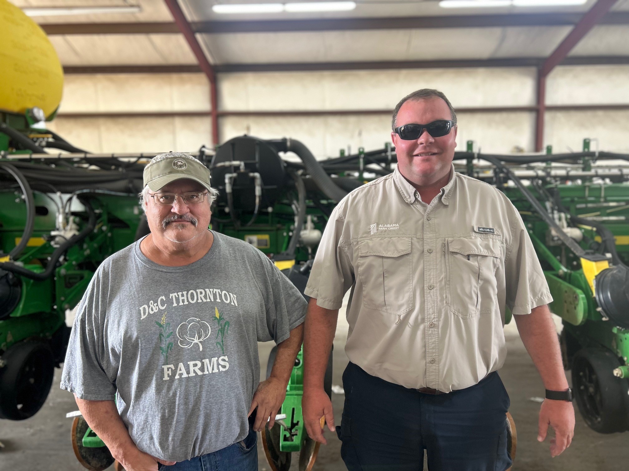 Two people in a garage standing in front of various farming equipment