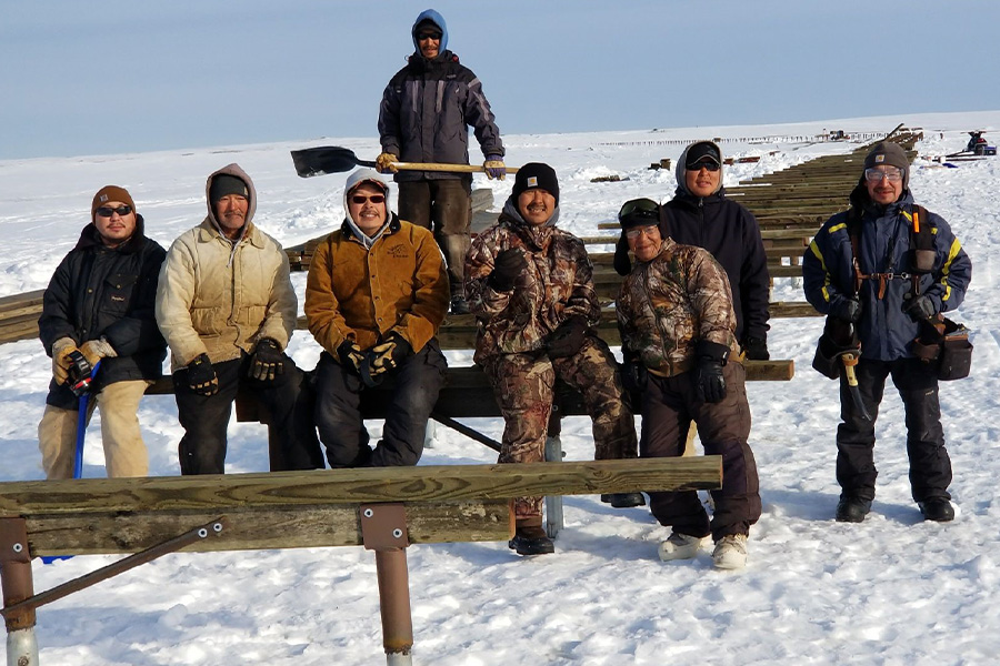 Eight people sitting on wood in a snow covered field