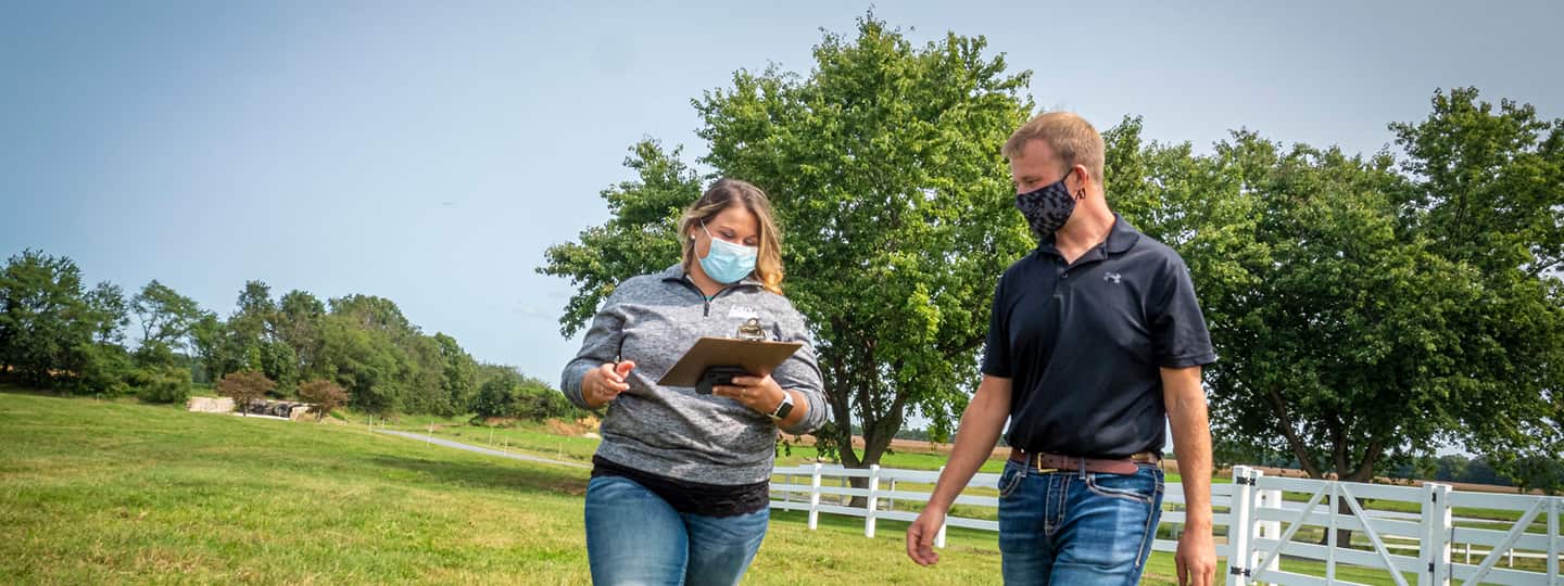 A farmer walks through a field with a USDA Service Center employee, with both wearing masks.