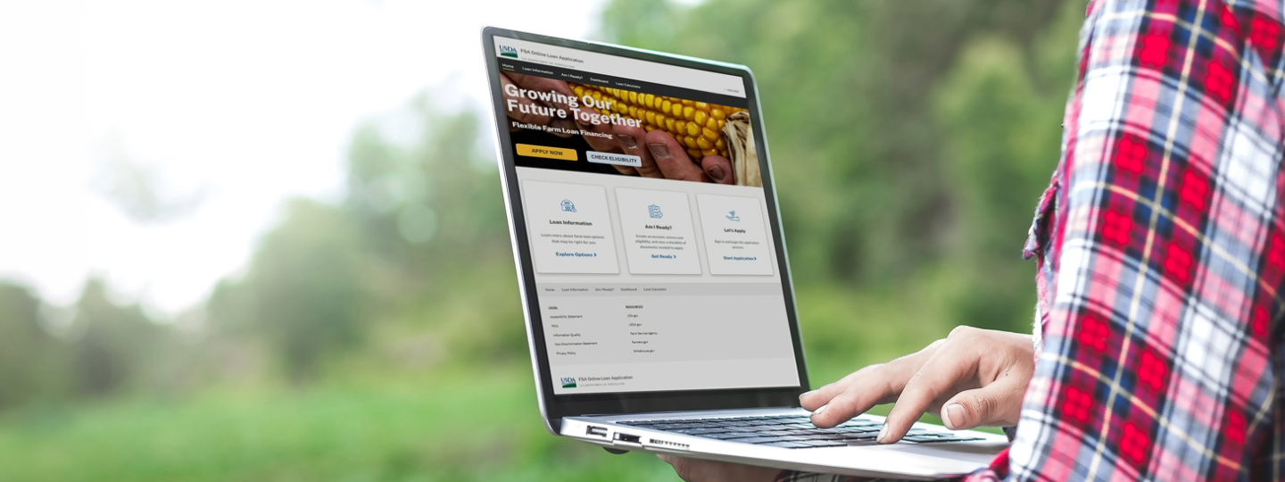 A person holds a laptop. The screen shows the new FSA online loan application website