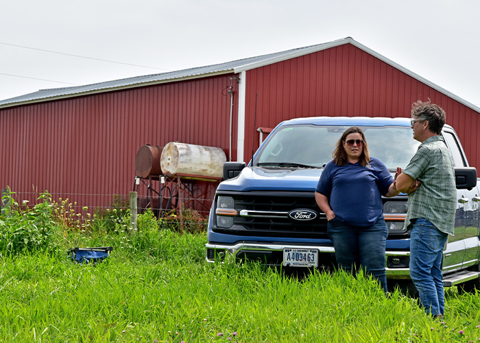 Two people standing in front of a pick-up truck next to a red barn