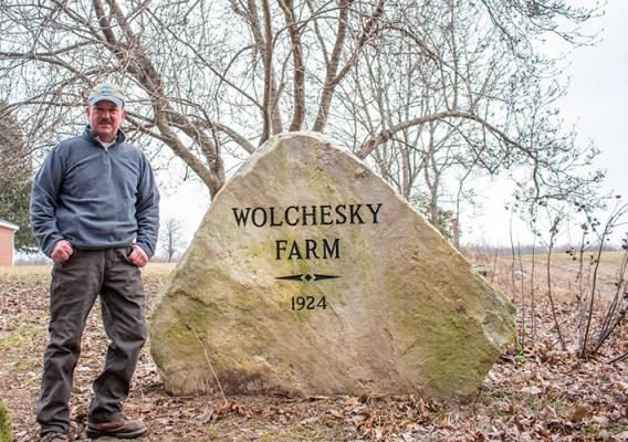 John Wolchesky, Jr. standing in front of his family rock for Wolchesky Farm.