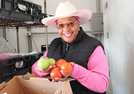 Dr. Cindy Ayers-Elliott is wearing sunglasses, a pink hat, and shirt with a black vest.  She is hold