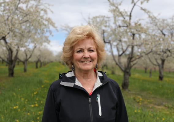 Lois Manigold standing on green grass with blooming trees in the background