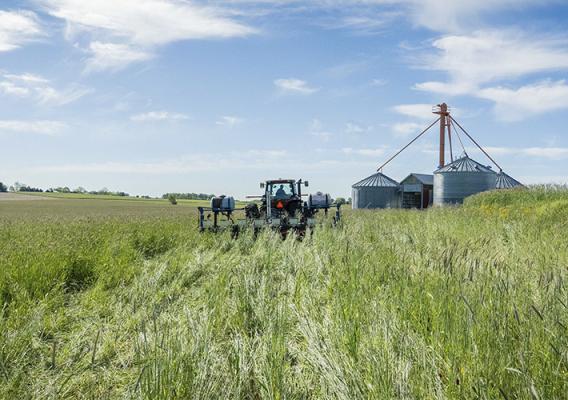 Tractor mowing tall grass with silos in the background