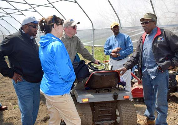 Five people standing around small tractor under a canopy