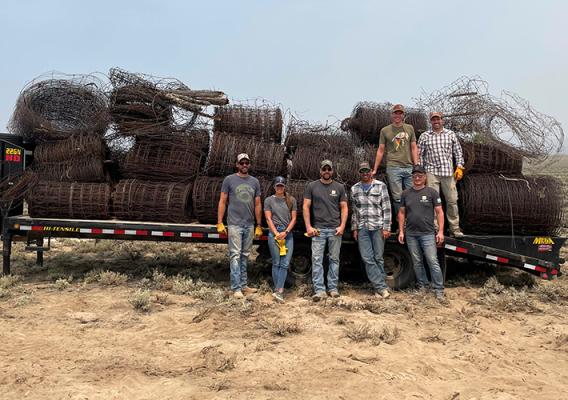 Seven people stand in front of coiled fencing on tuck bed