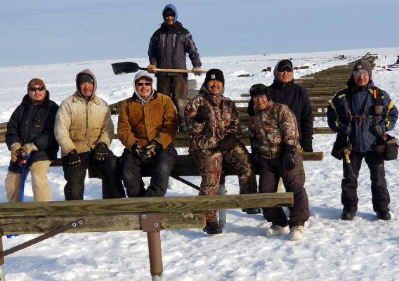 Eight people sitting on wood in a snow covered field