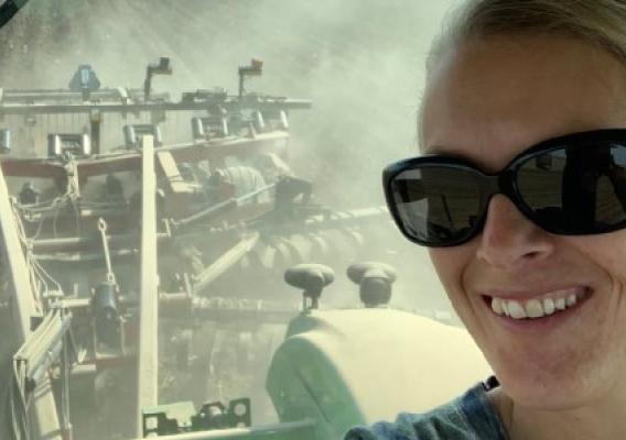smiling woman wearing sunglasses, sitting on a tractor