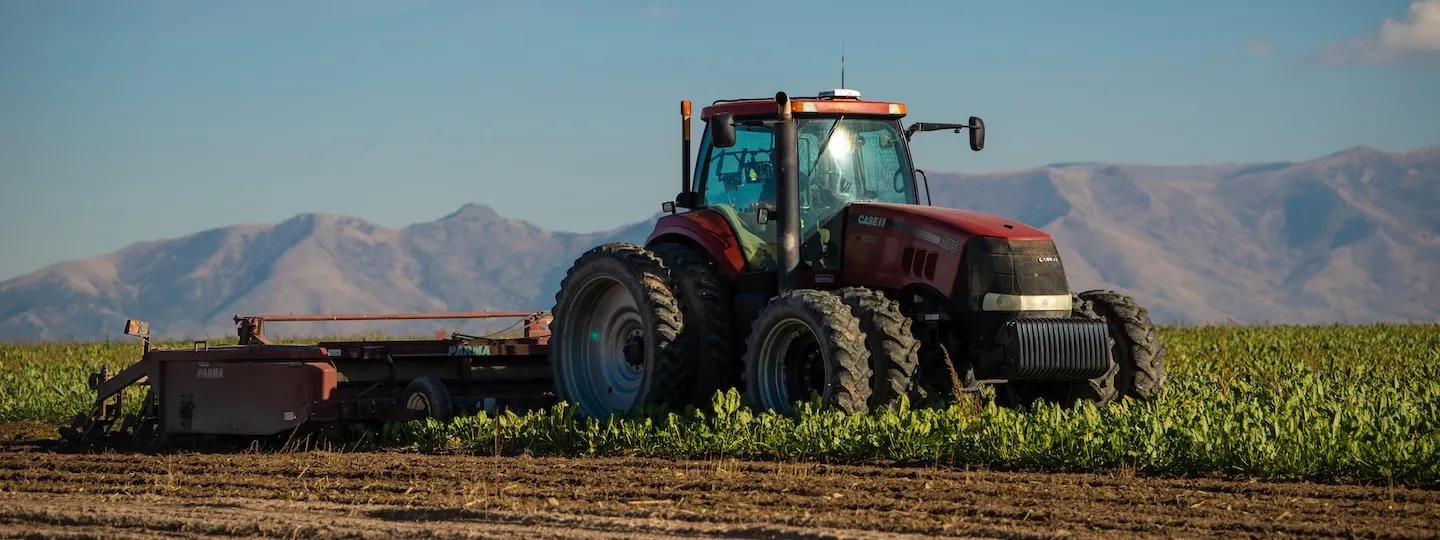 A modern red tractor plows a field against a background of mountains