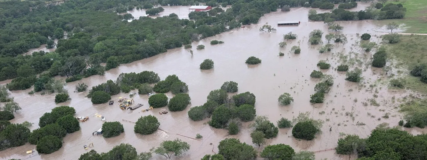 Aerial shot of flooded land with only tree tops peaking above brown water