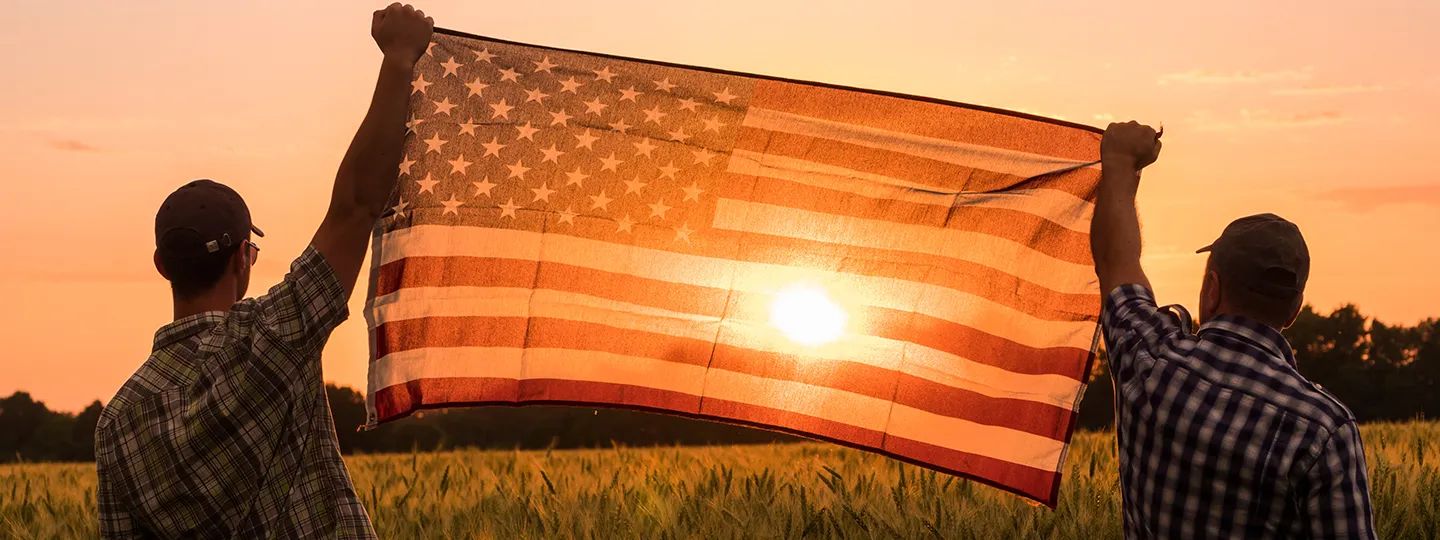 Two men hold the American flag up in a field