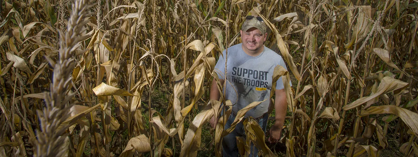 A man with a baseball cap and t-shirt reading &quot;support the troops&quot; stands in a field