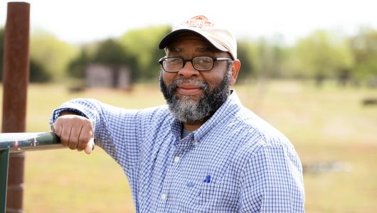 Person standing in a pasture with arm resting on metal gate