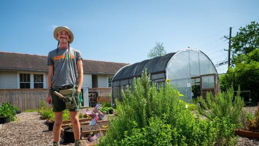Person standing in garden with high tunnel in background