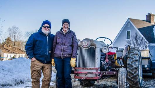 Two people standing in front of a vintage tractor