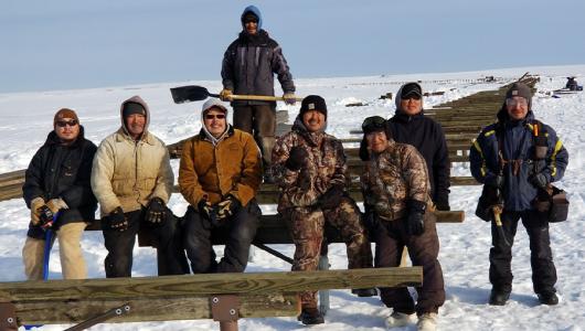 Eight people sitting on wood in a snow covered field