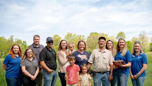 Thirteen people standing in a field smiling